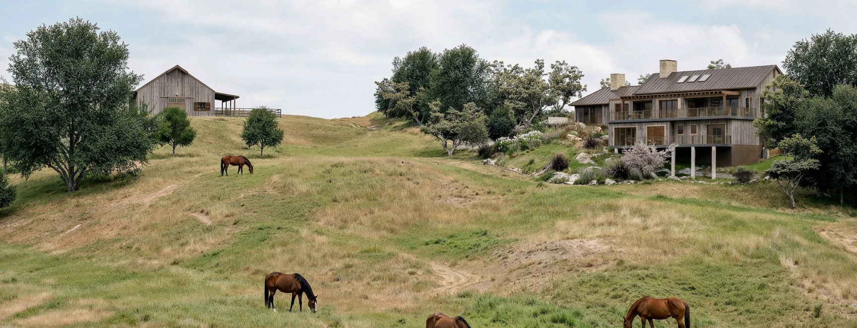 Timber homes set among oak trees and grazing horses on a rolling hillside